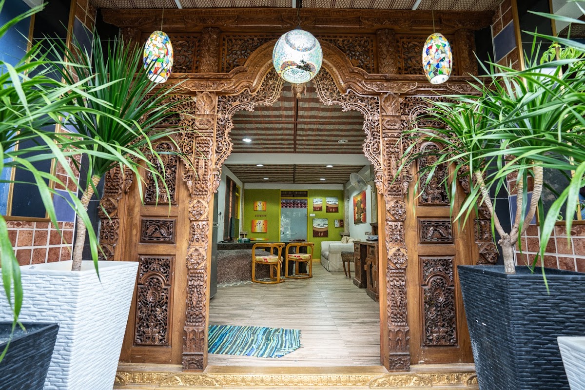 A hand-carved Balinese teak entrance archway with stained-glass hanging lanterns opening into a lime-green sitting room