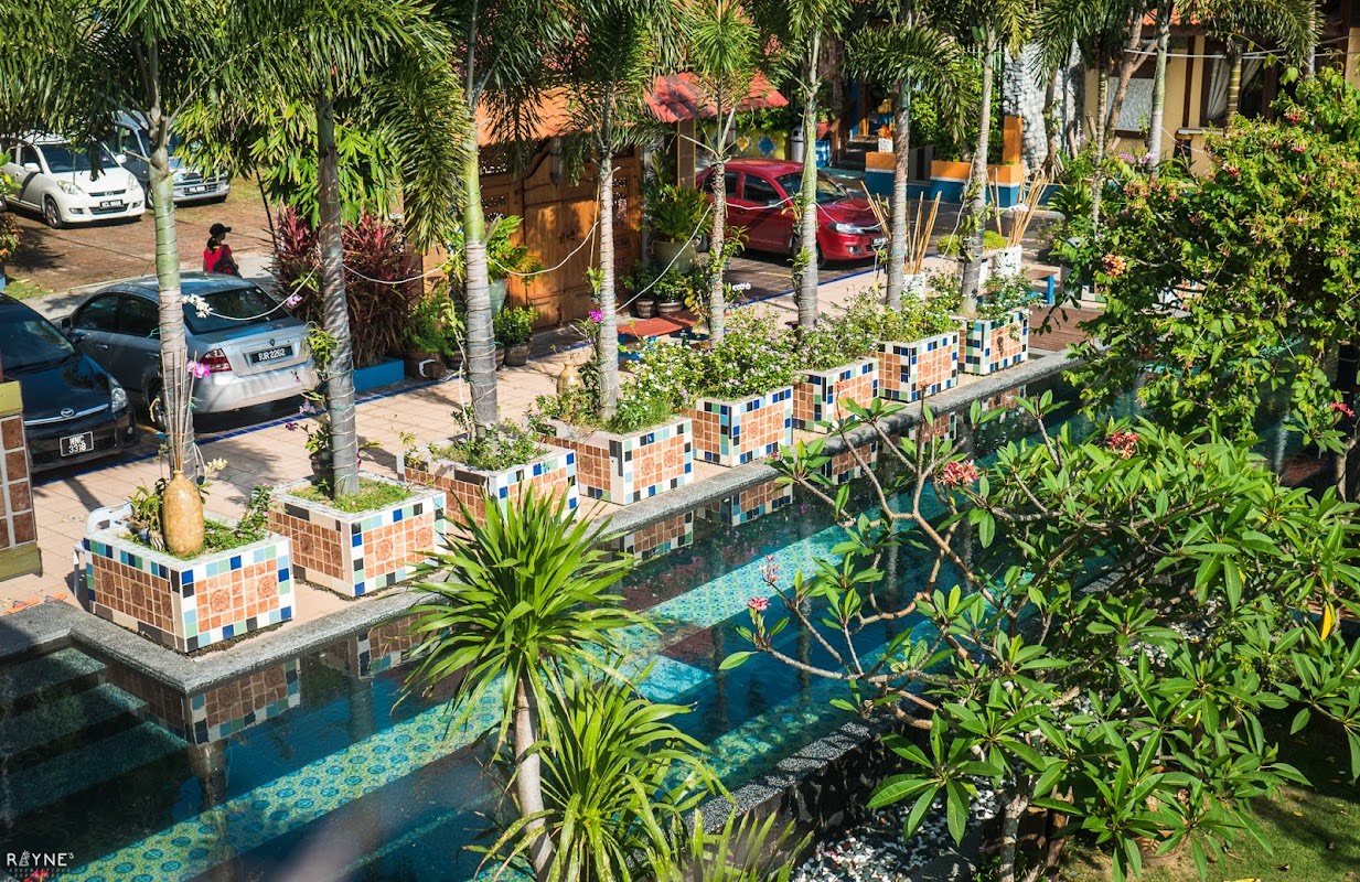 Aerial view of the resort pool flanked by orange-and-blue mosaic-tiled planters, palm trees and frangipani