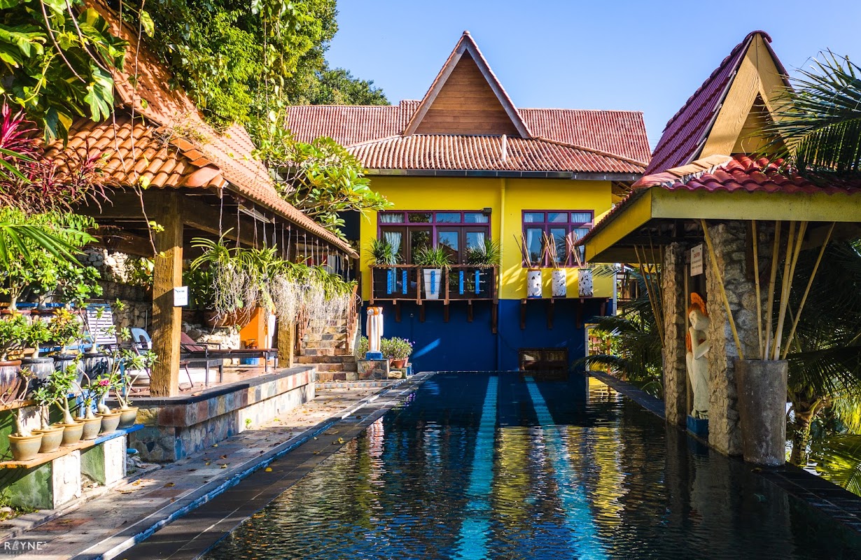 The infinity pool at Lost Paradise Resort, framed by saffron-yellow and cobalt-blue Balinese pavilions with terracotta roofs